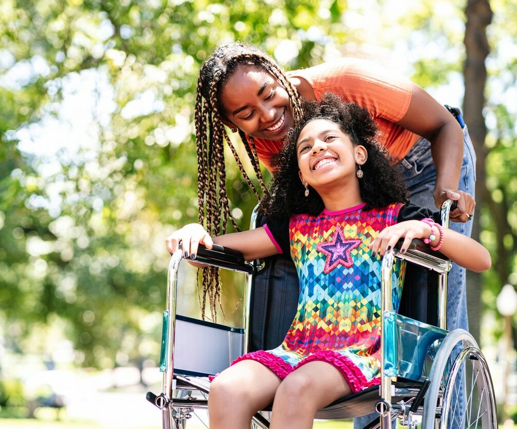 A little girl in a wheelchair enjoying a walk at the park with her mother.