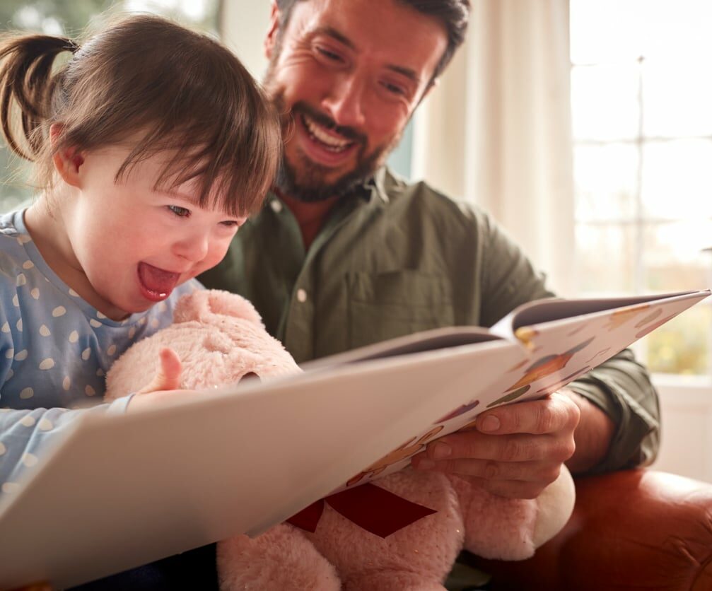 Father With Down Syndrome Daughter Reading Book At Home Together